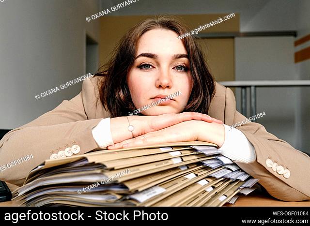 Young businesswoman leaning on stack of file at desk in office