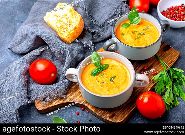 Homemade soup of fresh tomatoes, onions, garlic and herbs served with green basil in ceramic pots on a wooden serving board, selective focus