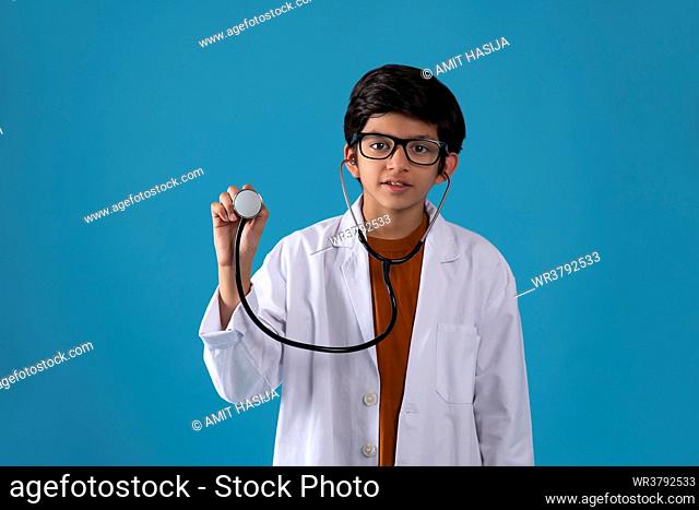 Portrait of smiling boy with stethoscope standing against blue background