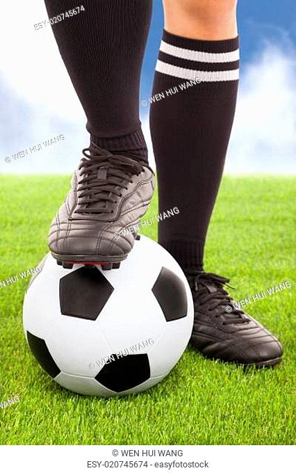 Soccer player's feet and football with sky background