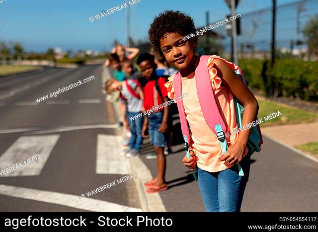 Front view close up of an African American schoolgirl wearing a pink t shirt and carrying a rucksack, looking for traffic while waiting to cross the road on the...