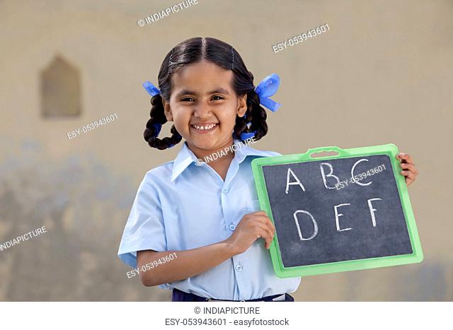Portrait of a cheerful girl in school uniform holding a slate