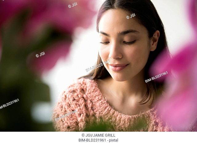 Pensive Hispanic woman behind pink flowers