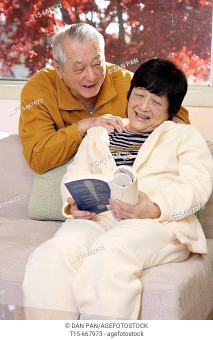 Senior Asian man giving his wife a massage while she reads
