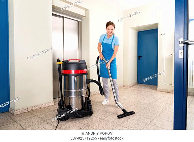 Young Female Janitor Cleaning Floor With Vacuum Cleaner