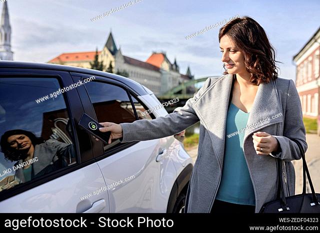Woman unlocking electric car through smart phone on sunny day