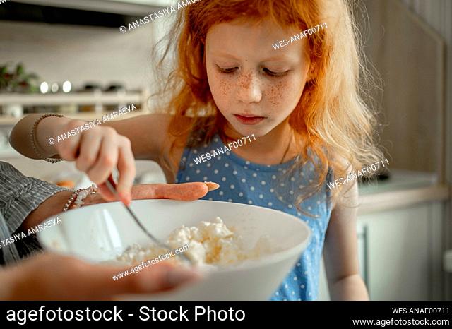 Redhead girl mixing cheese in bowl at home