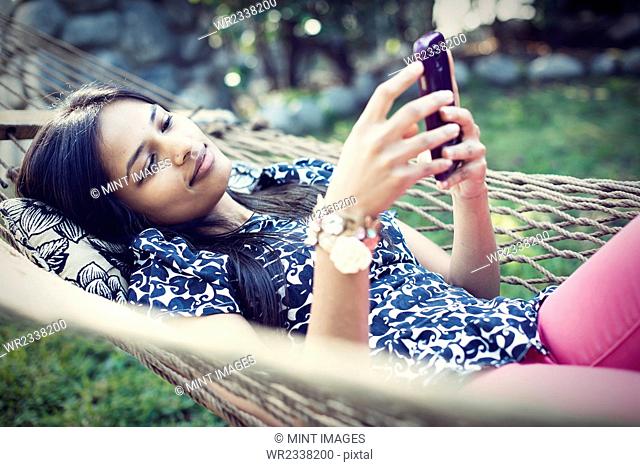 A woman lying in a garden hammock taking selfies with her phone
