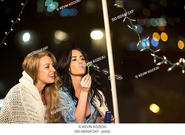Two female friends blowing bubbles at rooftop party