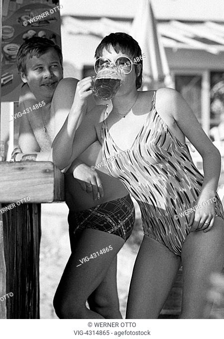 Seventies, black and white photo, holidays, tourism, young couple in bathing wear standing at a bar, girl drinks a beer, aged 25 to 30 years, Spain