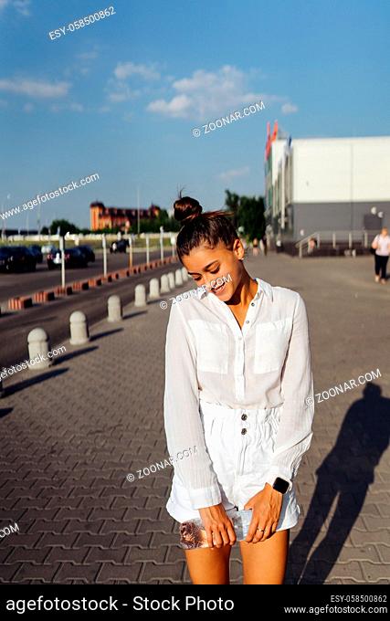Young woman posing at camera on the street in white clothes
