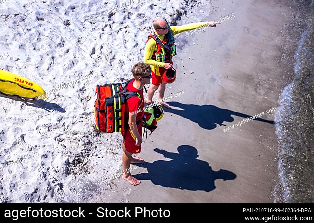 15 July 2021, Mecklenburg-Western Pomerania, Prerow: Lifeguards Nils Frechen and Nils Lerner from the DLRG water rescue team stand next to the pier on the beach...