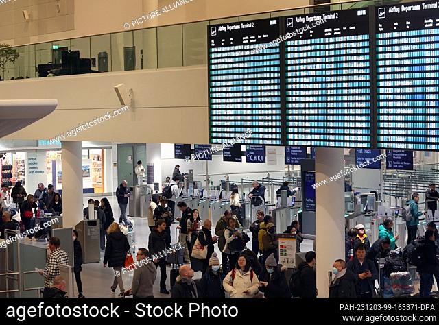 03 December 2023, Bavaria, Munich: Passengers stand under a display board at Munich Airport. Munich Airport resumed flight operations at 06:00 on Sunday