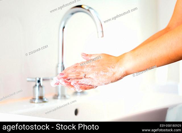 Woman washing hands with soap in bathroom with flowing water. Female cleaning under running water as virus prevention. Lady protecting herself from infection...