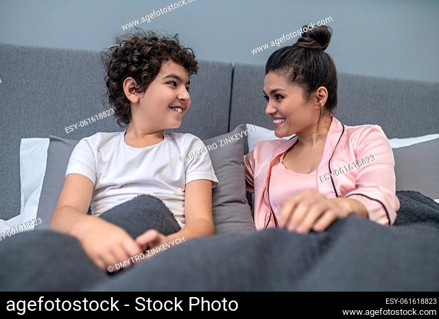 Happy morning. A cute curly-haired boy sitting in bed with his mom