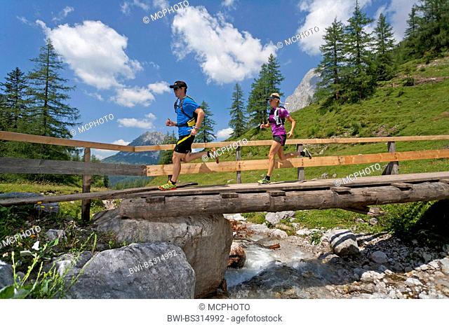 young couple running over a wooden bridge over a brook while trail running in the Dachstein Mountains, Austria, Styria, Dachstein