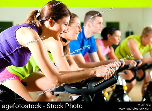Group of five people - men and women - spinning in gym or fitness club exercising their legs doing cardio training