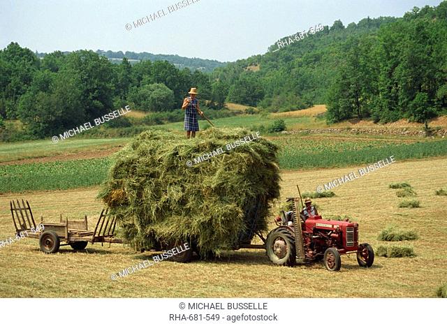 Farming couple with tractor and full trailer during haymaking in a field near Lalbenque, Lot, Midi Pyrenees, France, Europe