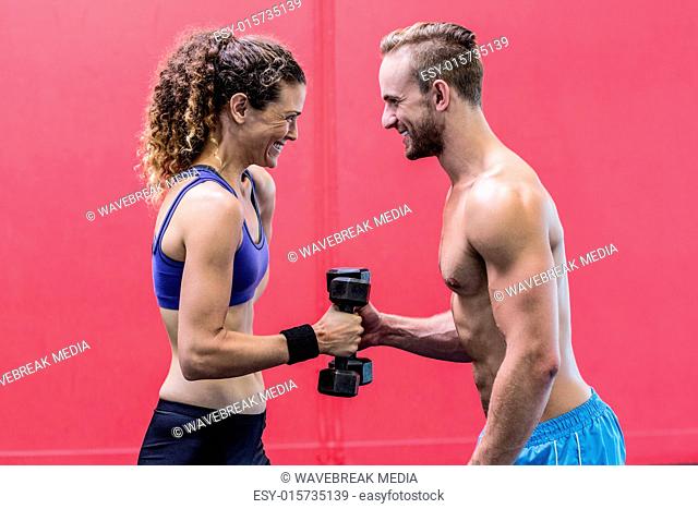 Laughing muscular couple lifting dumbbells