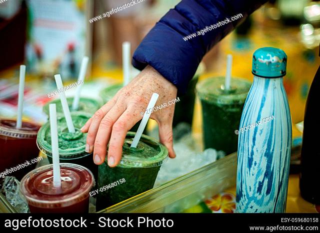 Green and red superfood smoothies are being displayed in a container full of ice in a farmer's market