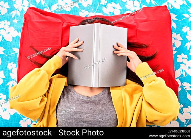 Ah, this read never seems to end. Young girl in her bed covering her face with an open book, as if she's really tired/bored of reading