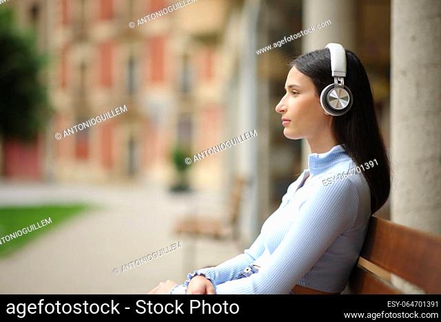 Side view portrait of a serious woman sitting in a bench listening to music