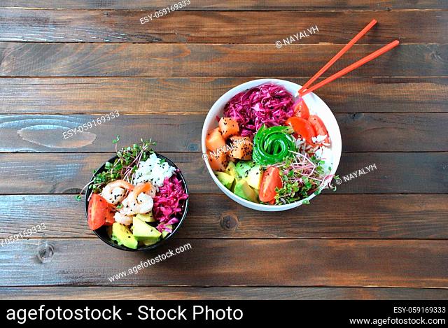 Organic food. Fresh seafood recipe. Two fresh poke bowls with salmon, shrimps, rice, red cabbage, avocado, cherry tomatoes and radish sprouts on wooden...