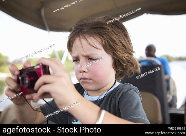 A five year old boy using his red camera, taking pictures on a river boat on the Zambezi River