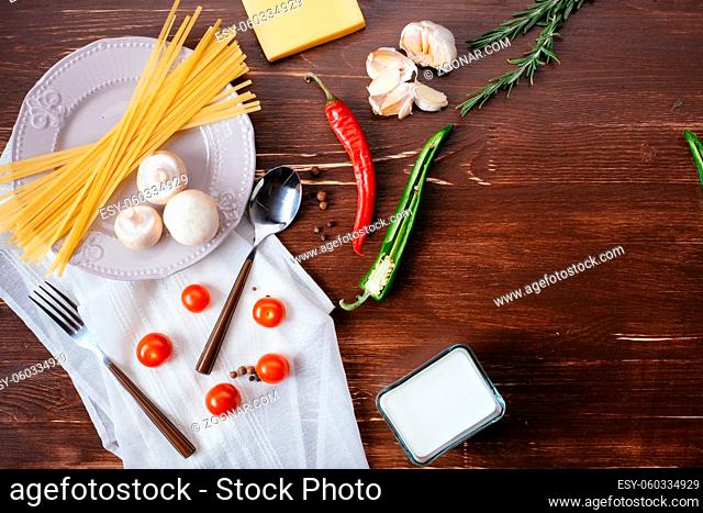 Ingredients for pasta on a wooden table. Plate, cutlery, pasta and fresh vegetables top view