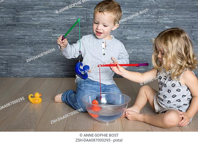 Children using toy fishing rods to catch rubber ducks floating in large bowl