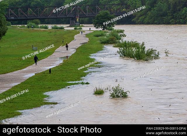 29 August 2023, Bavaria, Munich: Passers-by walk along the banks of the flooded Isar River, which flows through the Bavarian capital