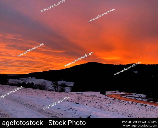 08 December 2023, Bavaria, Ahorntal: The sun rises over the Ahorntal valley in Franconian Switzerland. The light is reflected in the road leading out of the...