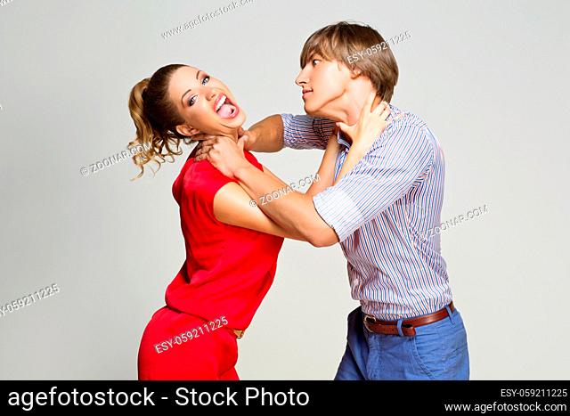 Couple strangling each other. Woman looking into camera. Over grey background