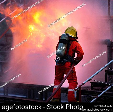 Firefighter using water fog type fire extinguisher to fighting with the fire flame from oil pipeline leak and explosion on oil rig and natural gas station