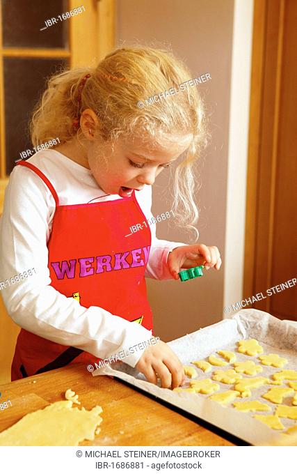 Baking Christmas cookies, girl putting cut out dough onto baking sheet
