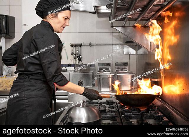 Woman Chef Cooking wok in the Kitchen. Cooking flaming wok with vegetables in the commercial kitchen. High quality photography