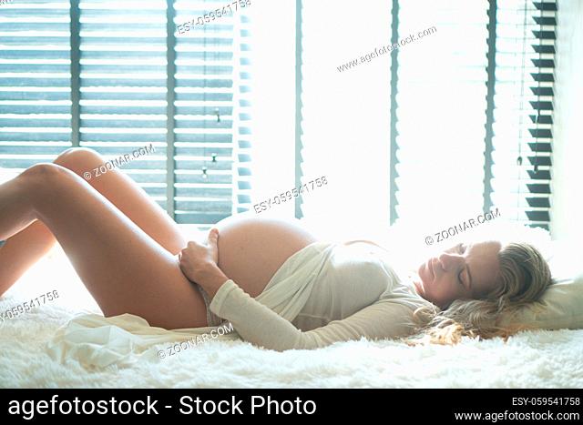 Side view of pregnant woman lying in bed and touching her belly at home