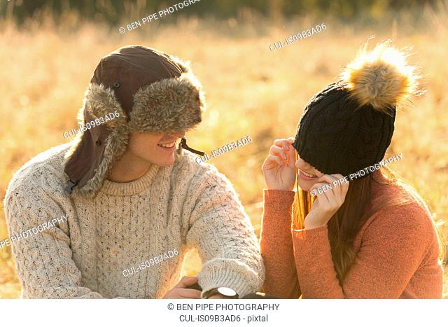 Young couple sitting in rural setting, wearing warm hats