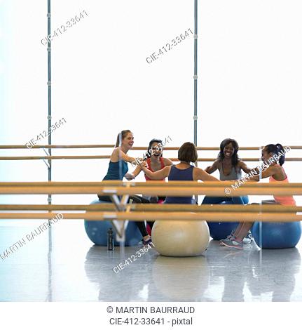 Smiling women holding hands on fitness balls in gym studio