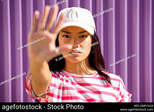 Young woman wearing cap gesturing in front of wall