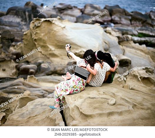 Three girls taking a photo of themselves while sitting on rock formations on Heping Island in Taiwan