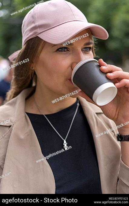 Beautiful young woman looking away while drinking coffee standing on street