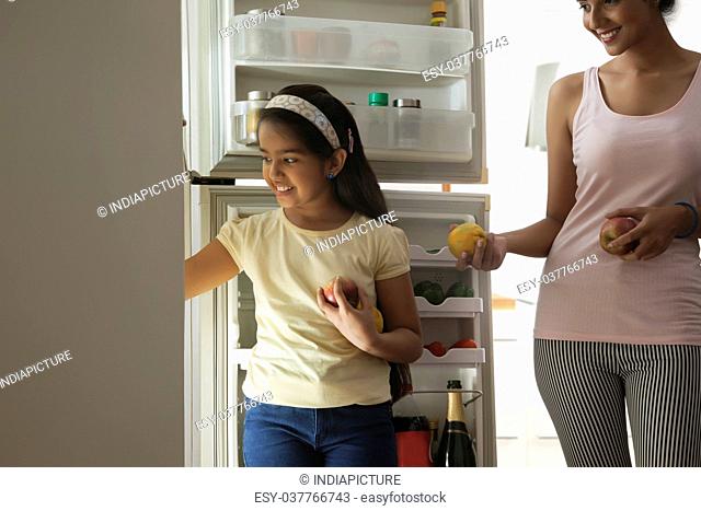 Close-up of daughter and mother putting fruits in refrigerator