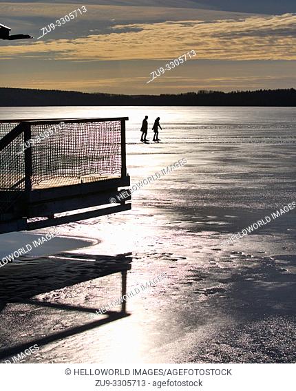 Two long distance ice skaters silhouetted in bright sunlight on Lake Malaren, Sigtuna, Sweden, Scandinavia