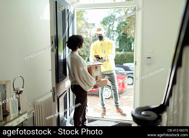 Woman receiving package from delivery man in face mask at front door