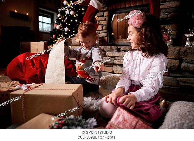 Young girl and boy sorting Christmas gifts, young boy rolling list