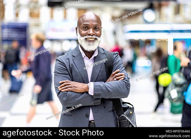 Smiling senior businessman with arms crossed at railroad station