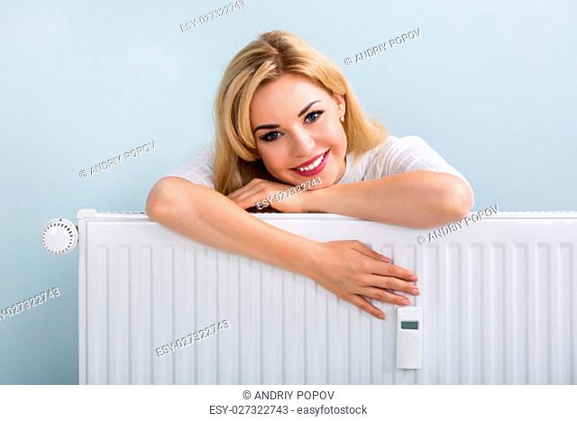 Young Happy Woman In Sweater Leaning On Radiator