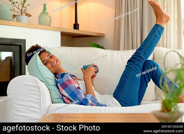 Mixed race woman sitting on couch drinking cup of coffee at home