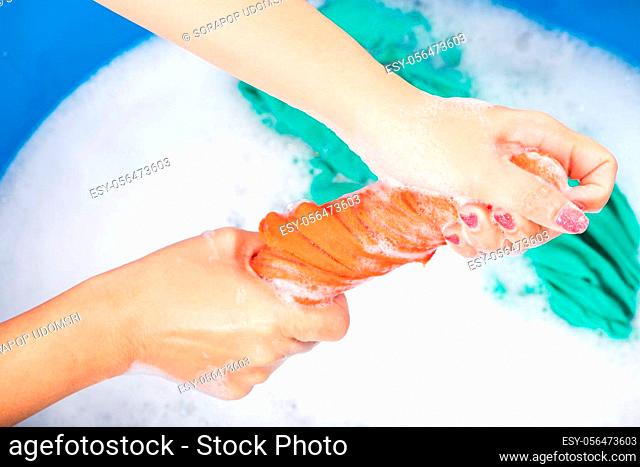 Closeup young Asian woman use hands washing color clothes in basin. Female squeeze wring out wet fabric cloth with detergent have soapy bubble in water